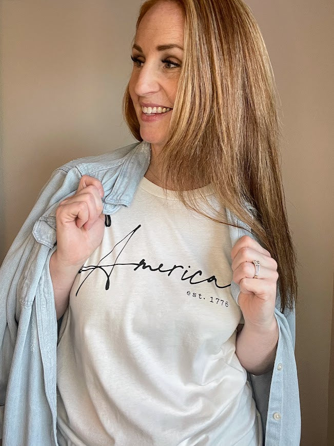Show your patriotic spirit with our "AMERICA EST. 1776" T-shirt. This hand-screen printed graphic tee proudly displays its message on a high-quality 100% cotton fabric, ensuring both style and comfort.